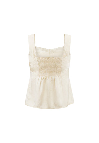 an-off-white-sleeveless-smocked-top-with-wide-shoulder-straps-and-a-ruffled-neckline-shown-against-a-plain-white-background