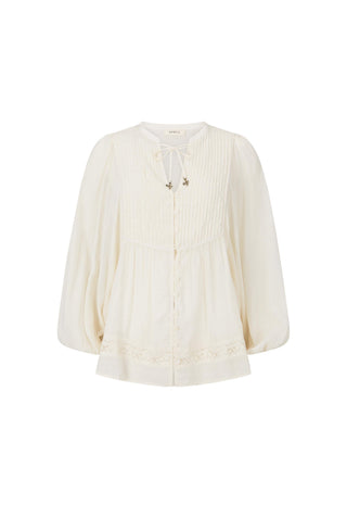 an-off-white-long-sleeve-blouse-with-a-tie-neck-detail-vertical-pleats-on-the-bodice-and-lace-trim-at-the-hem-shown-against-a-plain-white-background