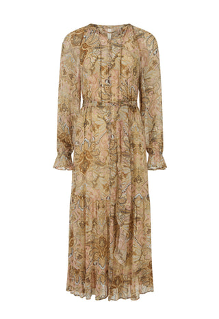 A woman outdoors in a grassy park wearing a flowing sheer boho-style maxi dress with an intricate paisley and floral pattern in warm beige