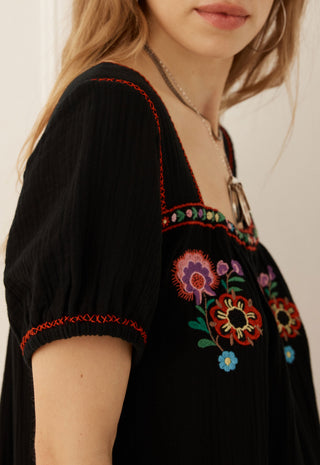 close-up-of-a-woman-wearing-a-black-short-sleeve-top-with-colorful-floral-embroidery-and-red-contrast-stitching-on-the-neckline-and-sleeve-cuffs