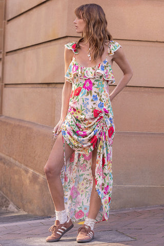 woman-wearing-a-colorful-floral-dress-standing-against-a-beige-wall