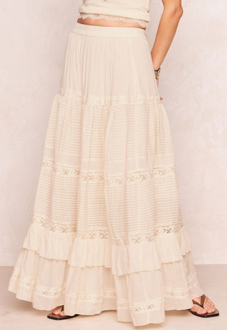a-long-cream-colored-tiered-maxi-skirt-with-delicate-lace-trim-and-ruffles-shown-on-a-model-from-the-waist-down-against-a-light-textured-wall