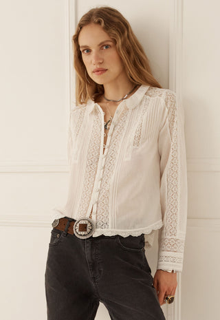 A woman wearing a white long-sleeve blouse with intricate lace and embroidered detailing