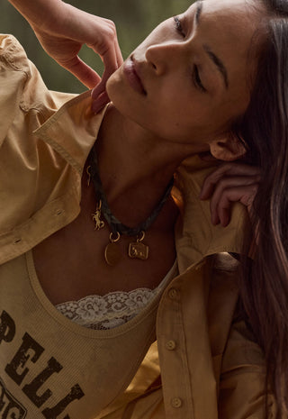 a-close-up-lifestyle-shot-of-a-woman-wearing-a-layered-necklace-set-the-set-includes-a-dark-green-braided-cord-necklace-with-a-small-gold-charms